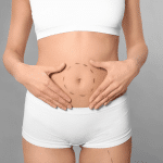 A woman putting her hands on her stomach, thinking about whether she should get a Tummy Tuck surgery or not
