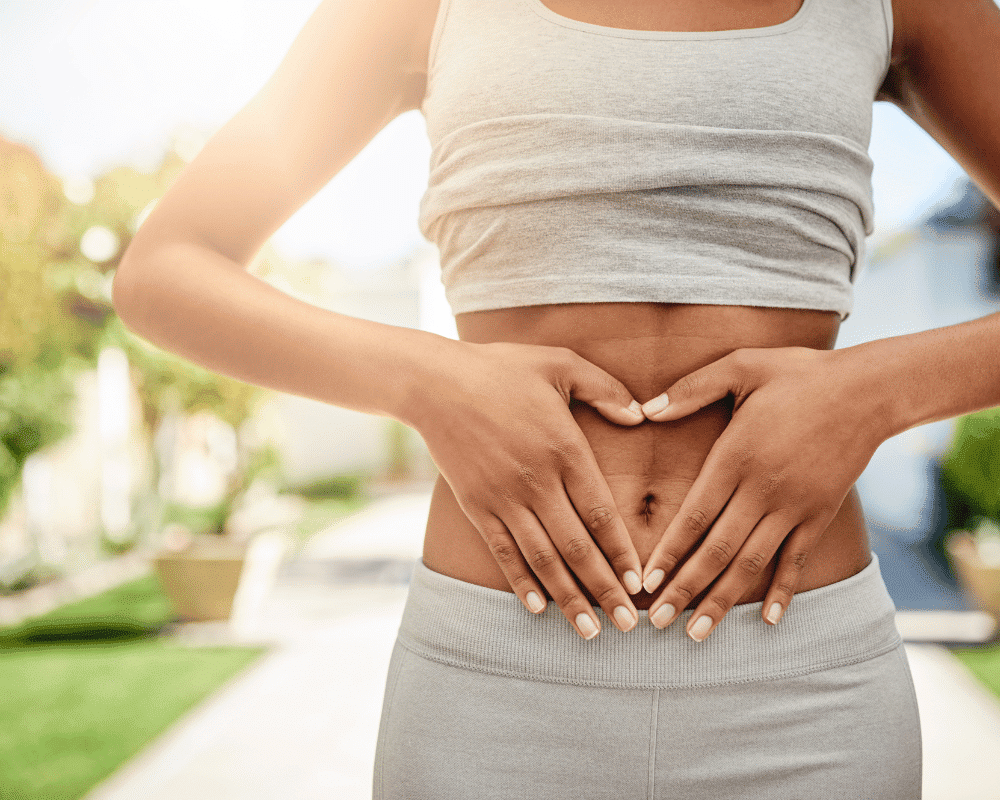 A woman putting her hands on her stomach, while thinking either she should get a tummy tuck surgery